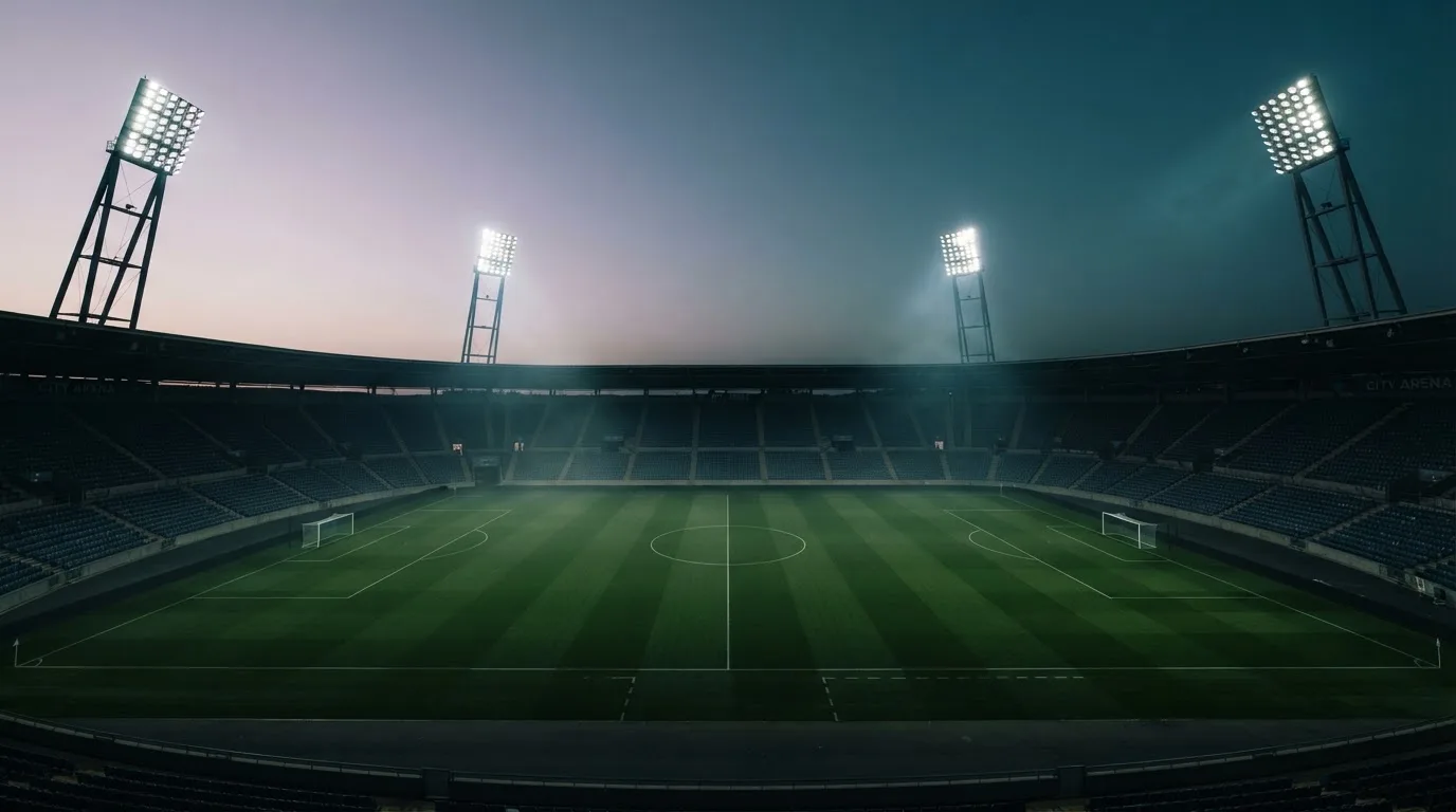 An empty football stadium with floodlight masts at dusk